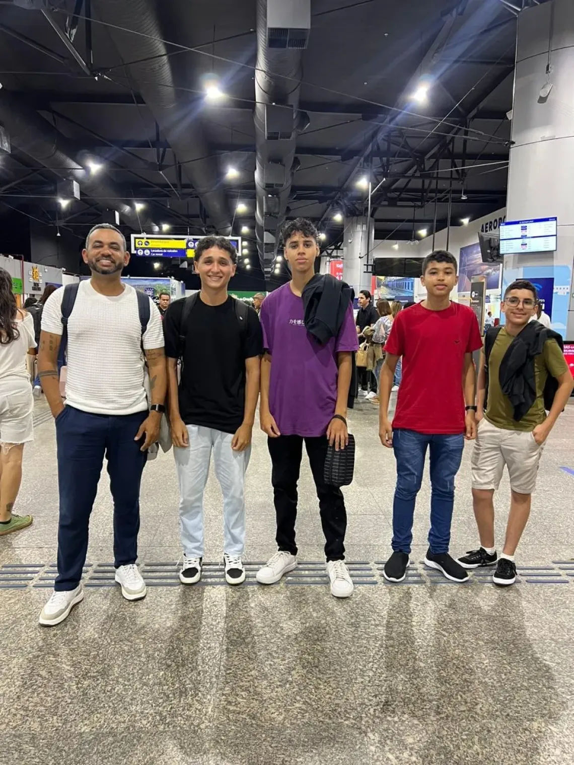 A group of young boys smiling as they stand in the airport