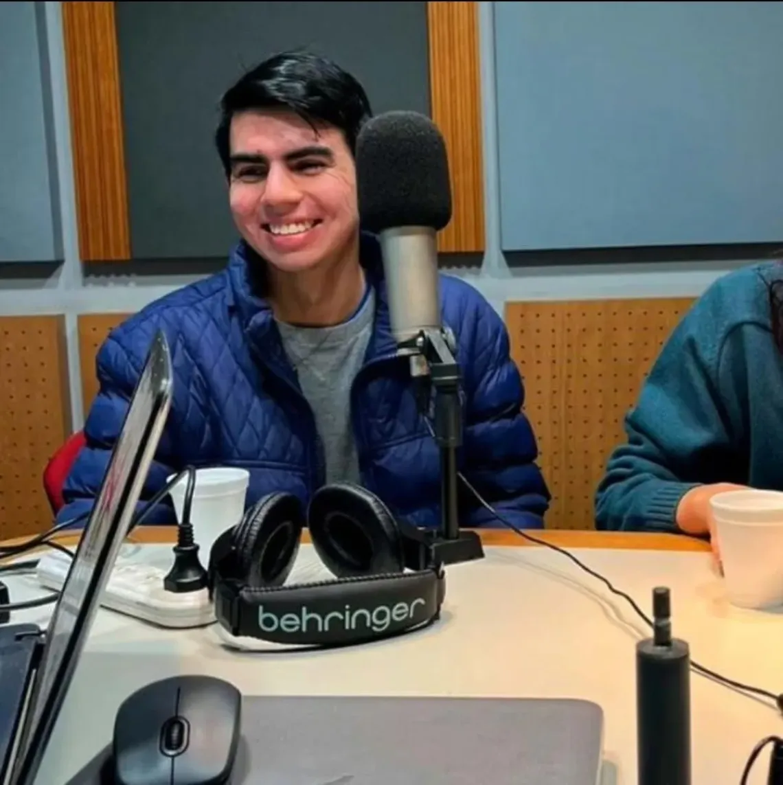 A photograph of a young man sitting behind a microphone in a radio studio