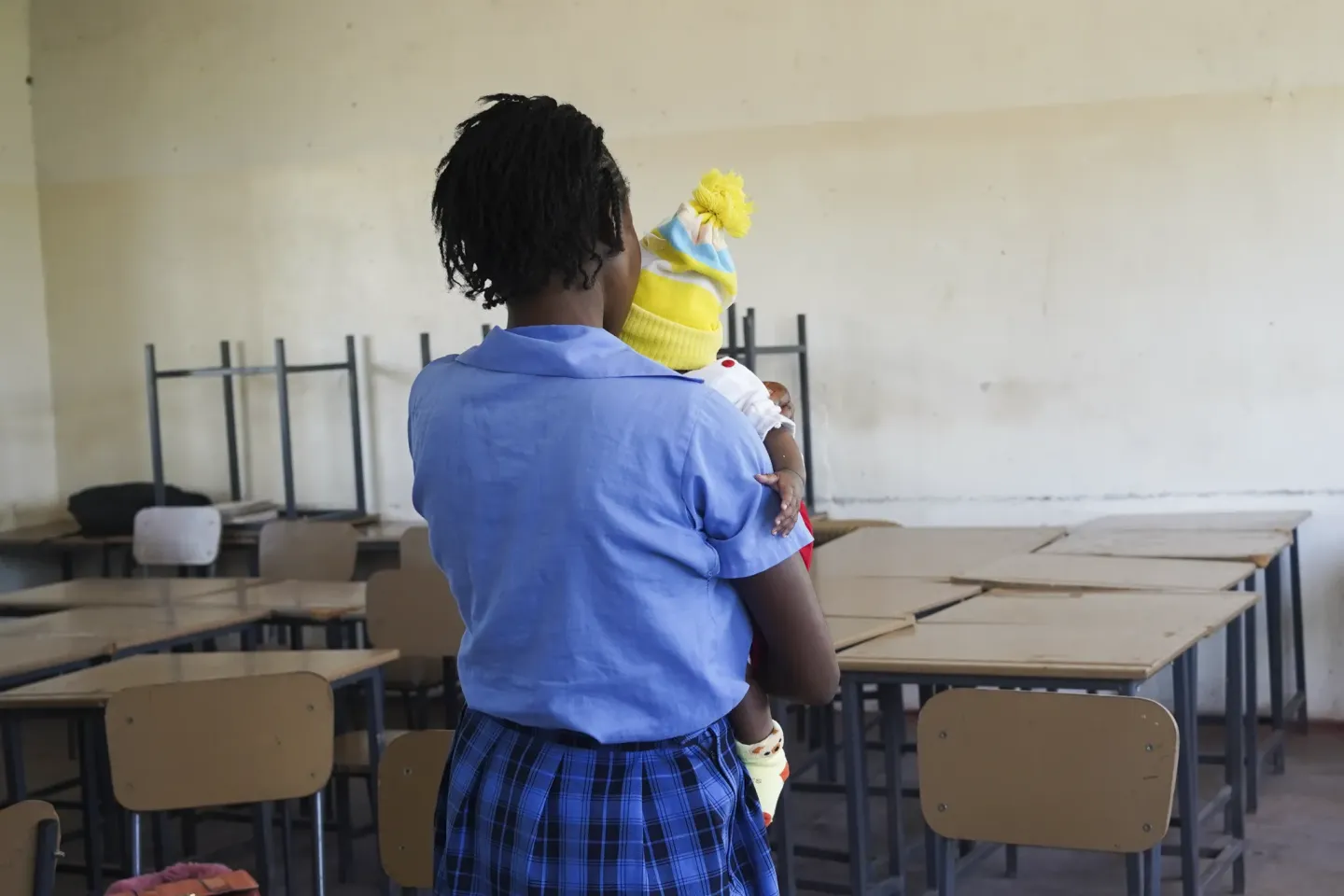 Person holding a young child while seated in a classroom at Mansa Secondary School, Luapula Province.