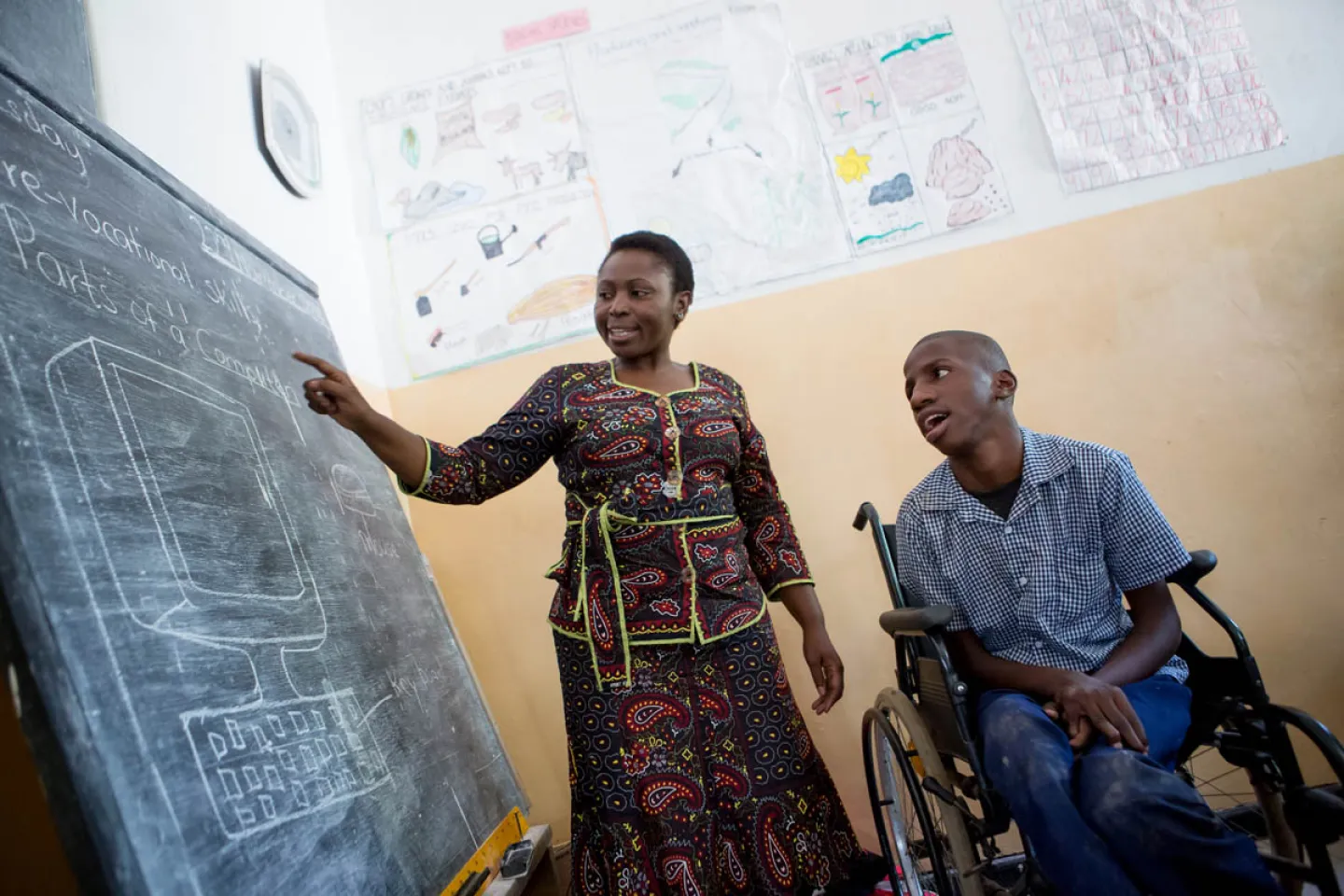 A teacher points to a black board with a student in a wheelchair