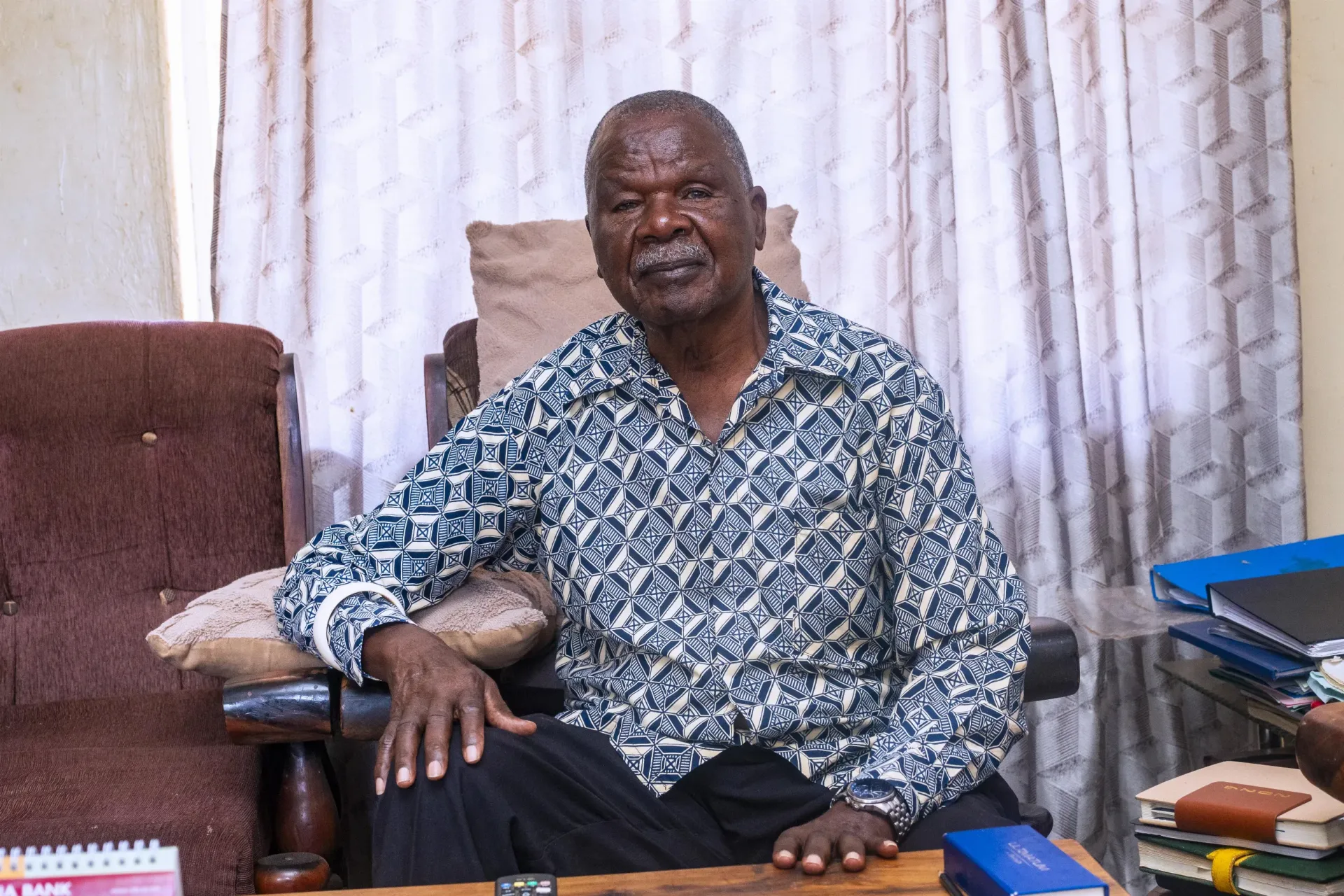 Elderly man seated indoors for a portrait.