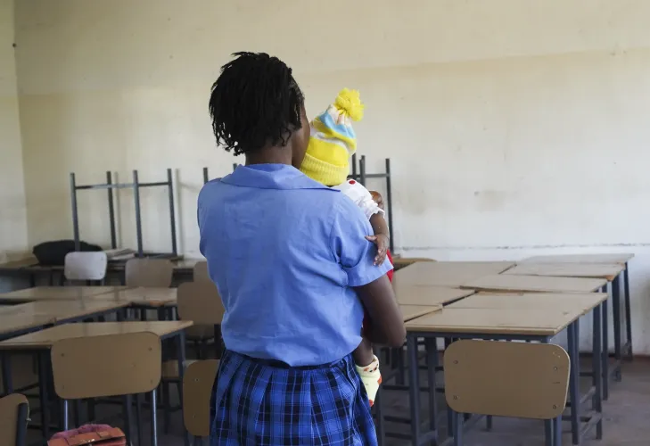 Person holding a young child while seated in a classroom at Mansa Secondary School, Luapula Province.