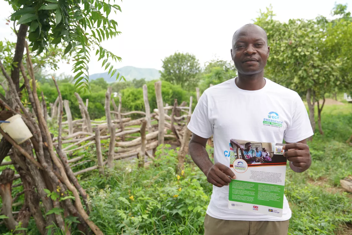 A community volunteer in a white T-shirt holds up an Emergency Cash Transfer poster