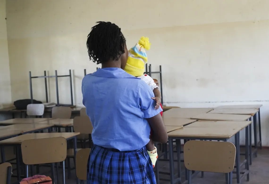 Person holding a young child while seated in a classroom at Mansa Secondary School, Luapula Province.