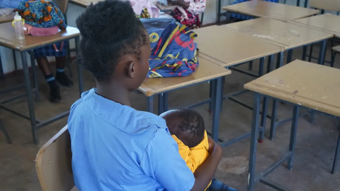 Person holding a young child while seated in a classroom at Mansa Secondary School, Luapula Province.