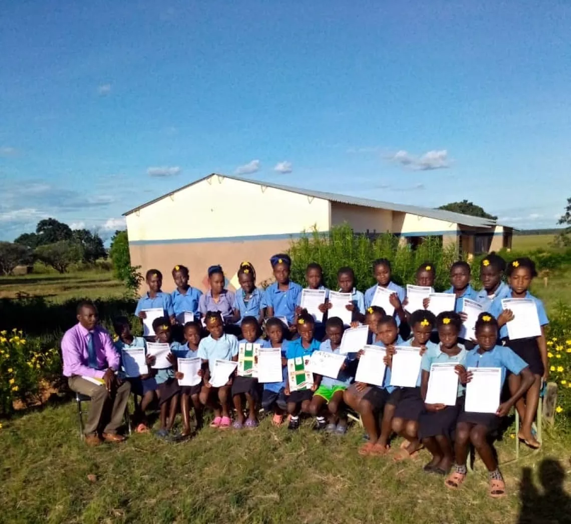 Mr. Musonda poses with his Grade 4 learners. The learners are holding new learning materials shared during the Catch-Up training.