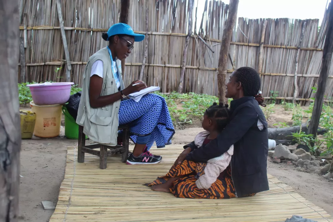 Two women are seated with a baby, engaging in conversation.
