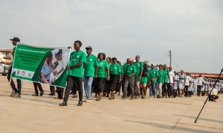 A group of community members and health workers march in Mansa during the launch of the malaria vaccine into Zambia&rsquo;s routine immunisation schedule. Participants wear green shirts and carry a banner promoting the malaria vaccine rollout, symbolising national unity and health awareness.